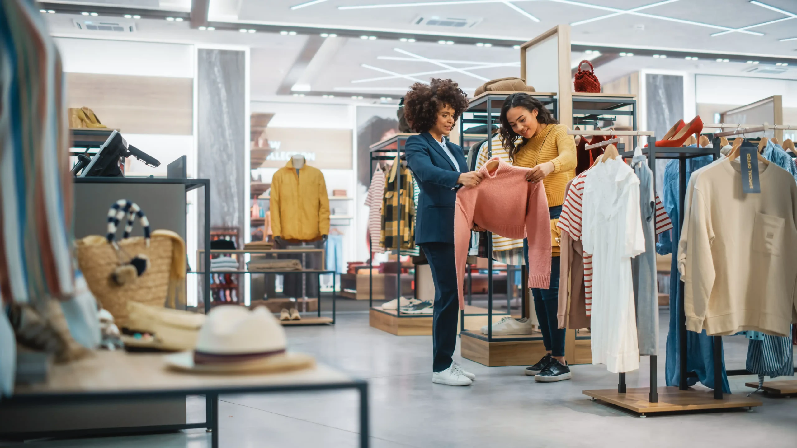 two women in a clothing store looking at a sweater they've pulled off the rack