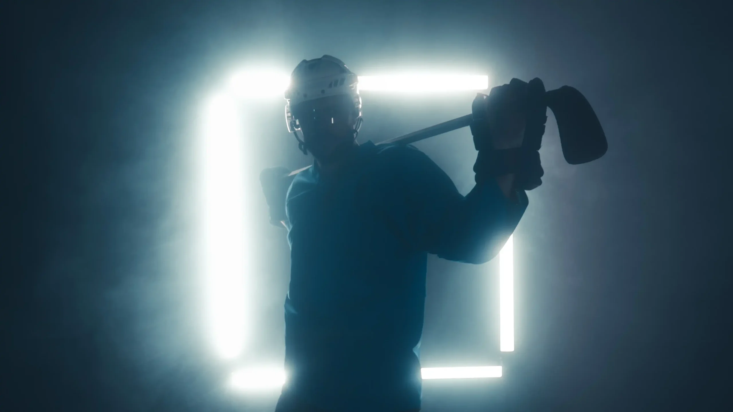 Backlit hockey player holding stick across shoulders