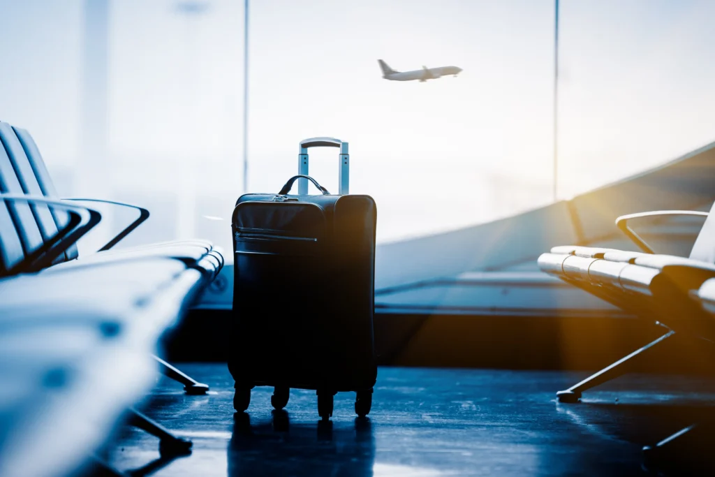 wheeled luggage sitting near airport window with plane in background