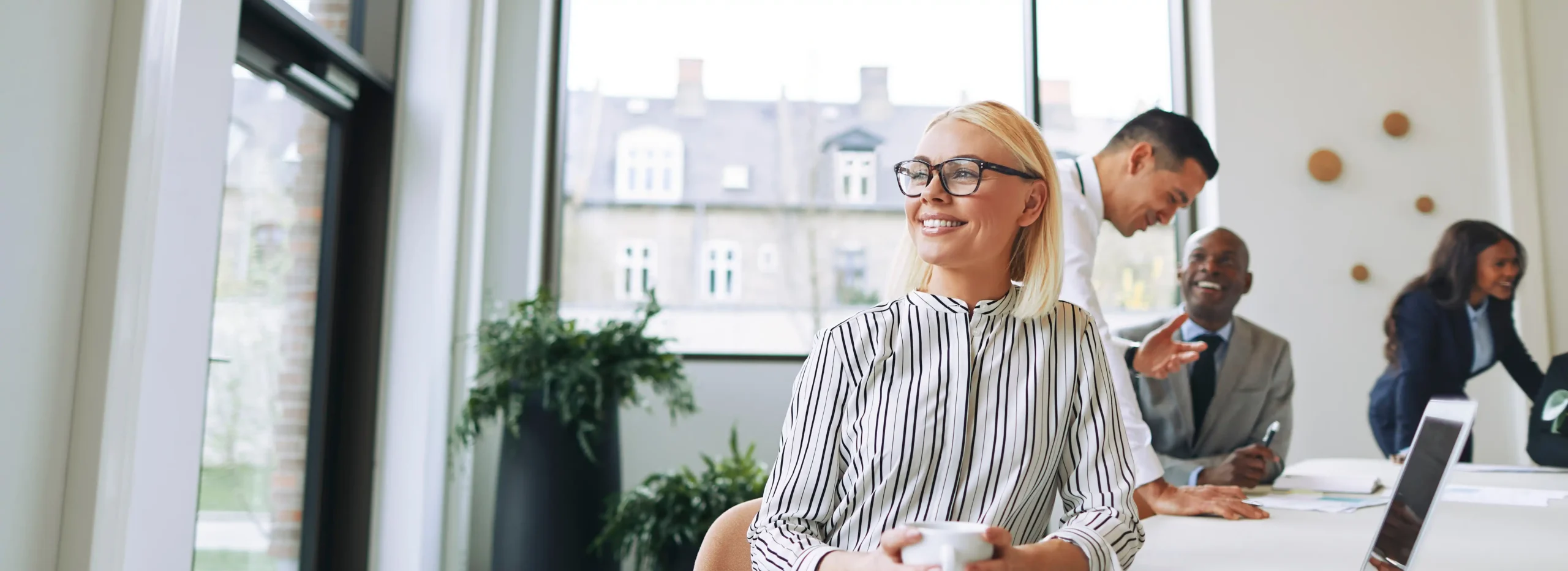 professional in open office smiling while looking out window with mug